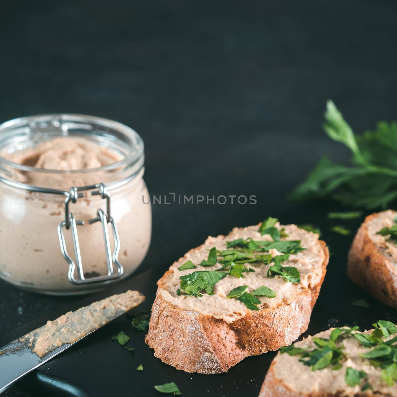 Close up view of slice bread with homemade turkey pate and fresh green parsley on black kutting board over black cement background, Copy space.