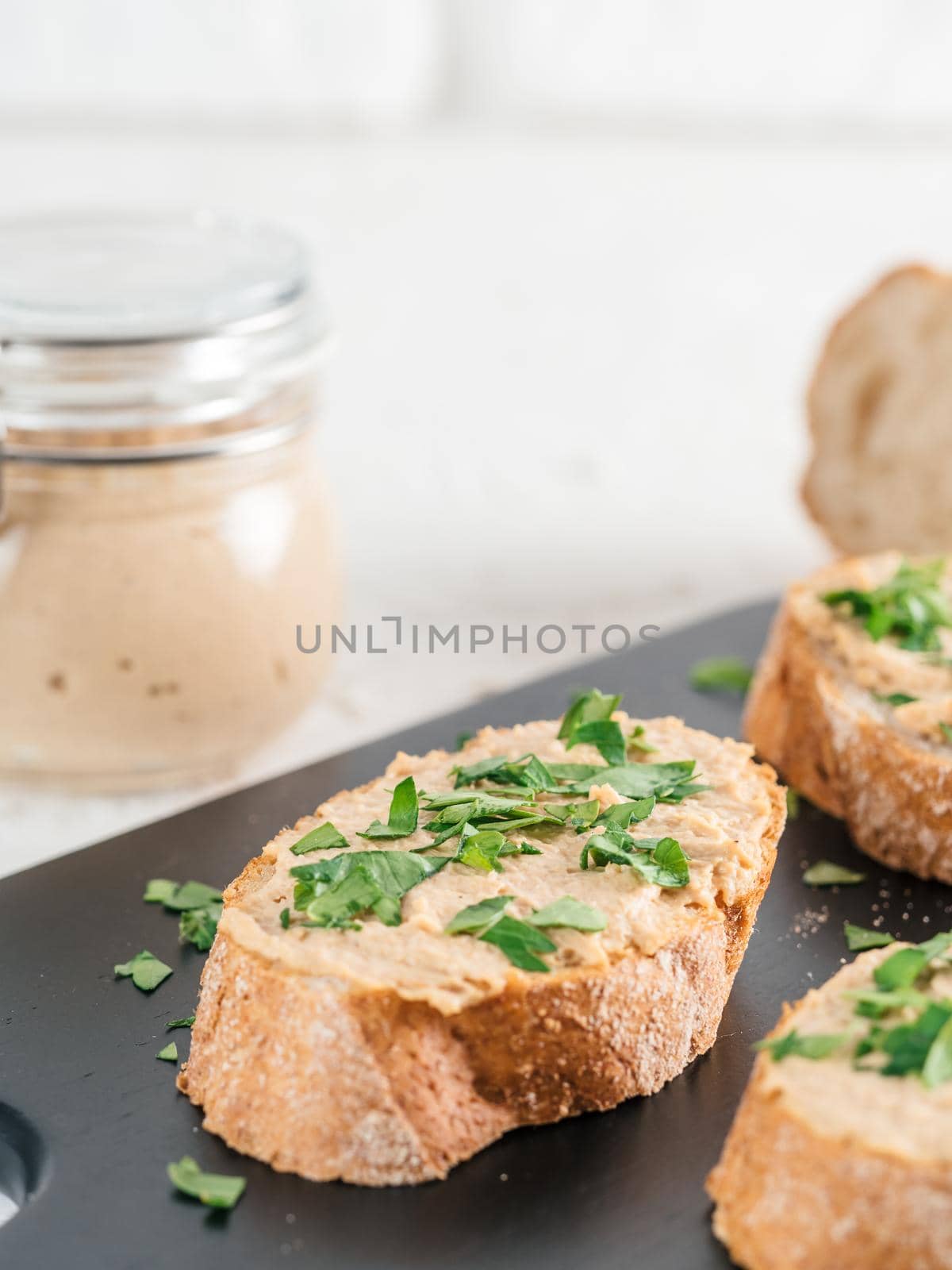 Close up view of slice bread with homemade turkey pate and fresh green parsley on black kutting board over white concrete background, Copy space.