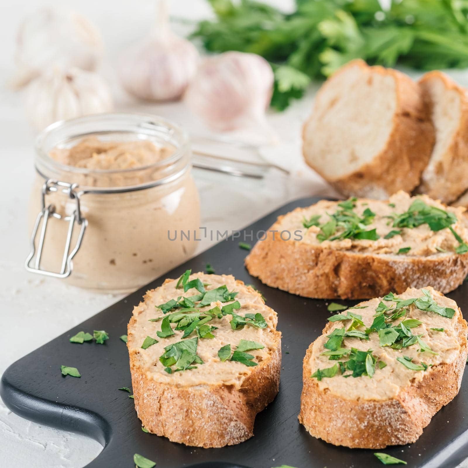 Close up view of slice bread with homemade turkey pate and fresh green parsley on black kutting board over white concrete background, Shallow DOF. Selective focus
