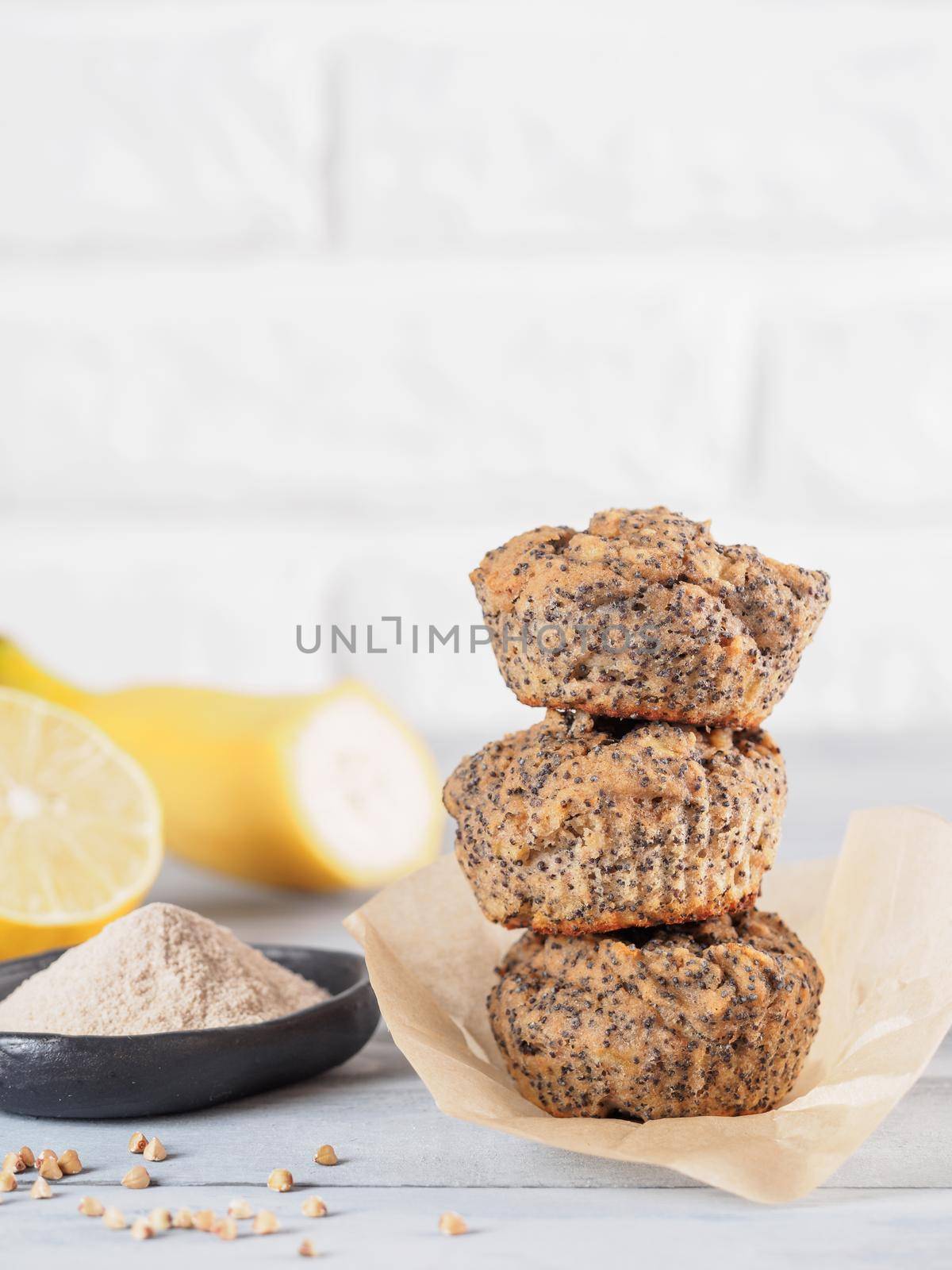 Healthy gluten-free homemmade banana muffins with buckwheat flour. Stack of three vegan muffins with poppy seeds and lemon on gray wooden table. Copy space