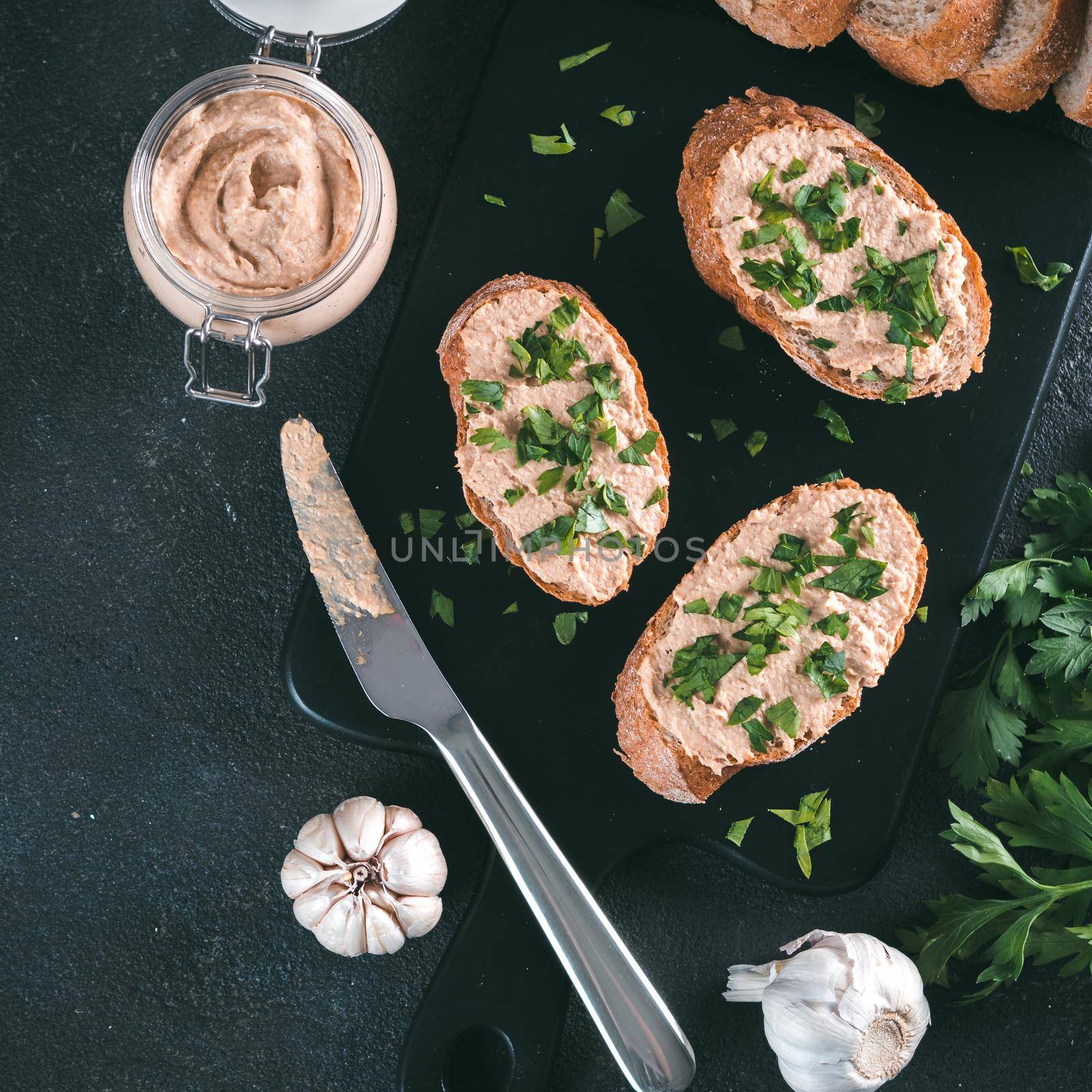 Top view of slice bread with homemade turkey pate and fresh green parsley on black kutting board over black cement background,
