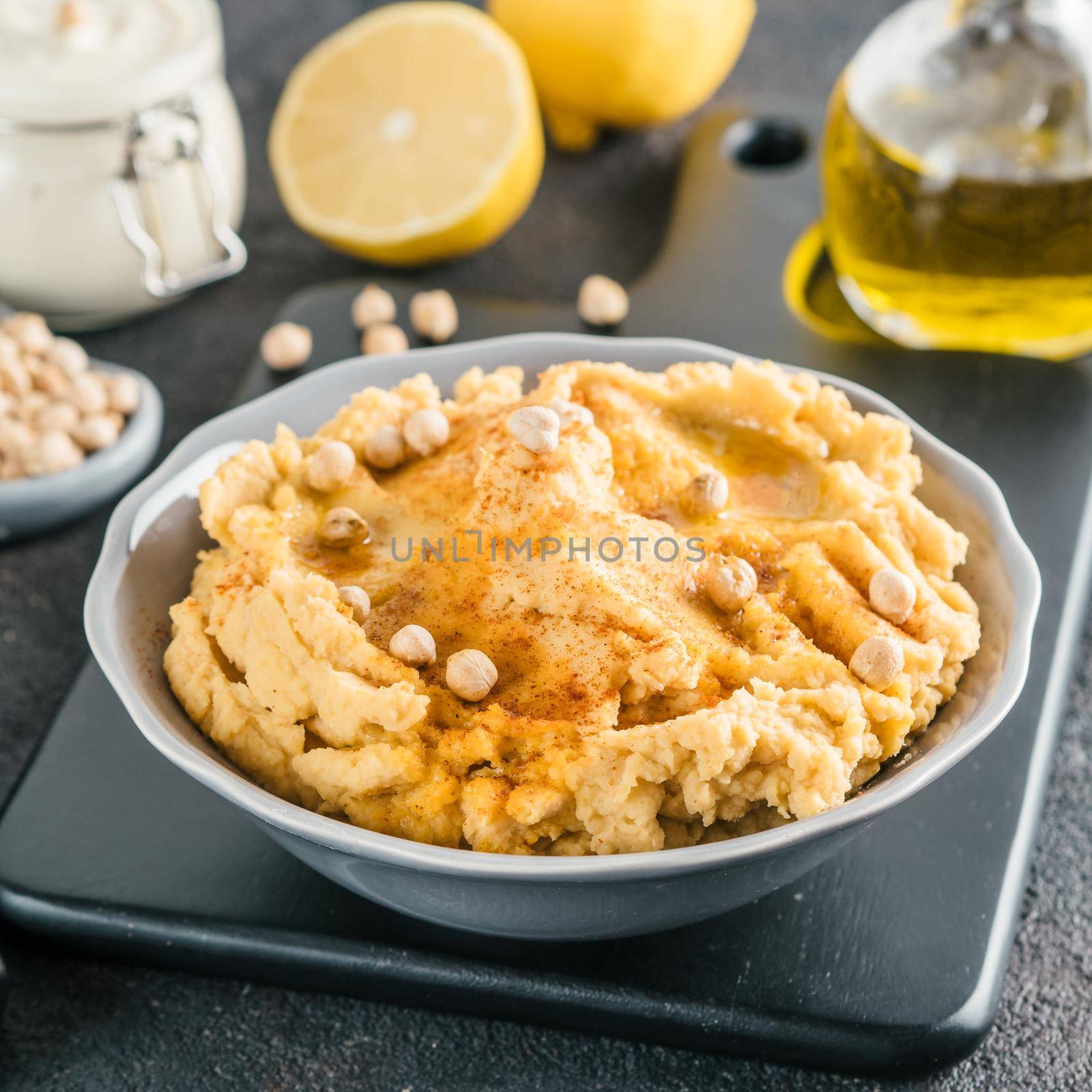Homemade hummus with olive oil in gray bowl and ingredients. Traditional middle eastern appetizer hummus on gray background - healthy vegan paste snack. Vegetarian diet,nutrition protein food concept