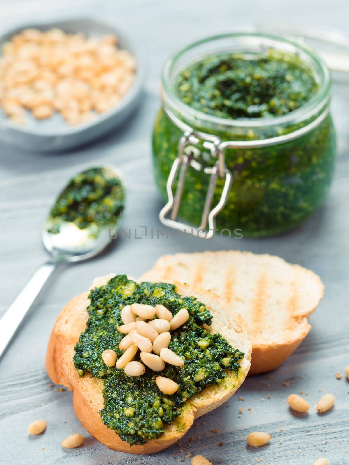 Close up view of baguette bread with fresh basil pesto sauce on gray wooden table. Copy space.