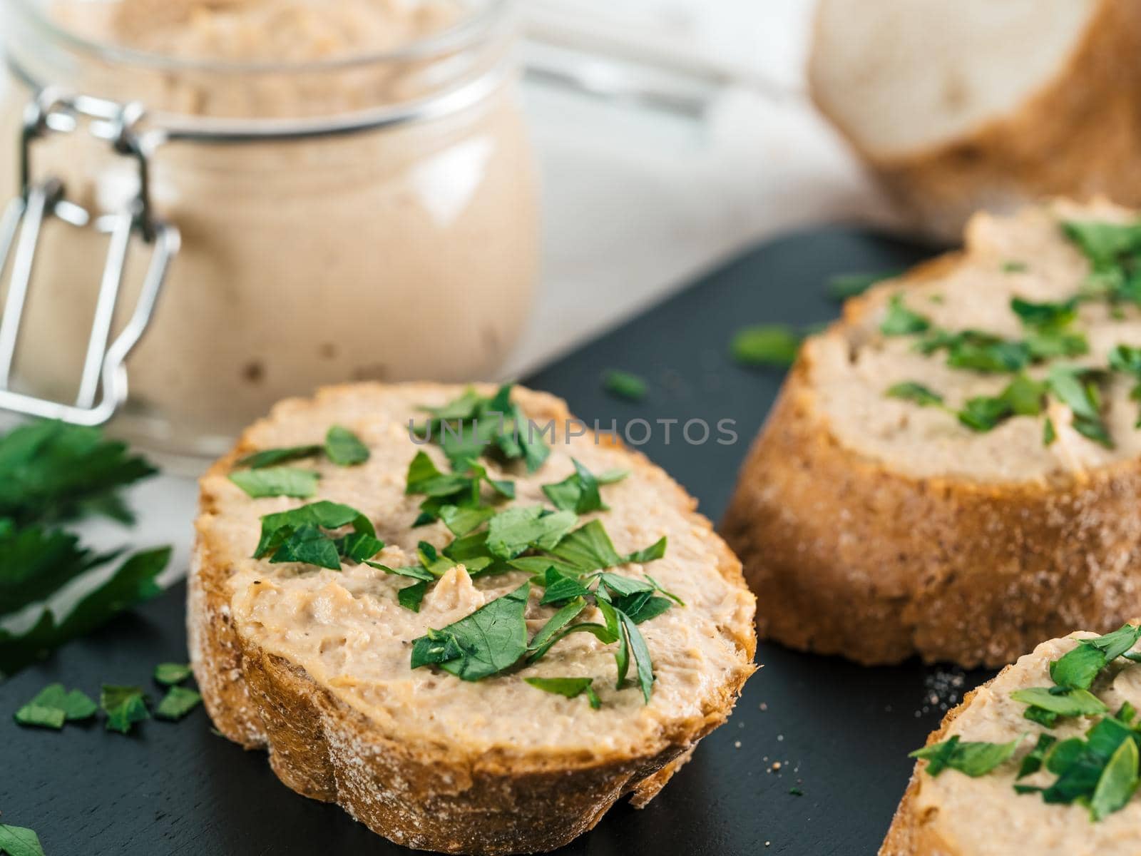 Close up view of slice bread with homemade turkey pate and fresh green parsley on black kutting board over white concrete background, Shallow DOF. Selective focus