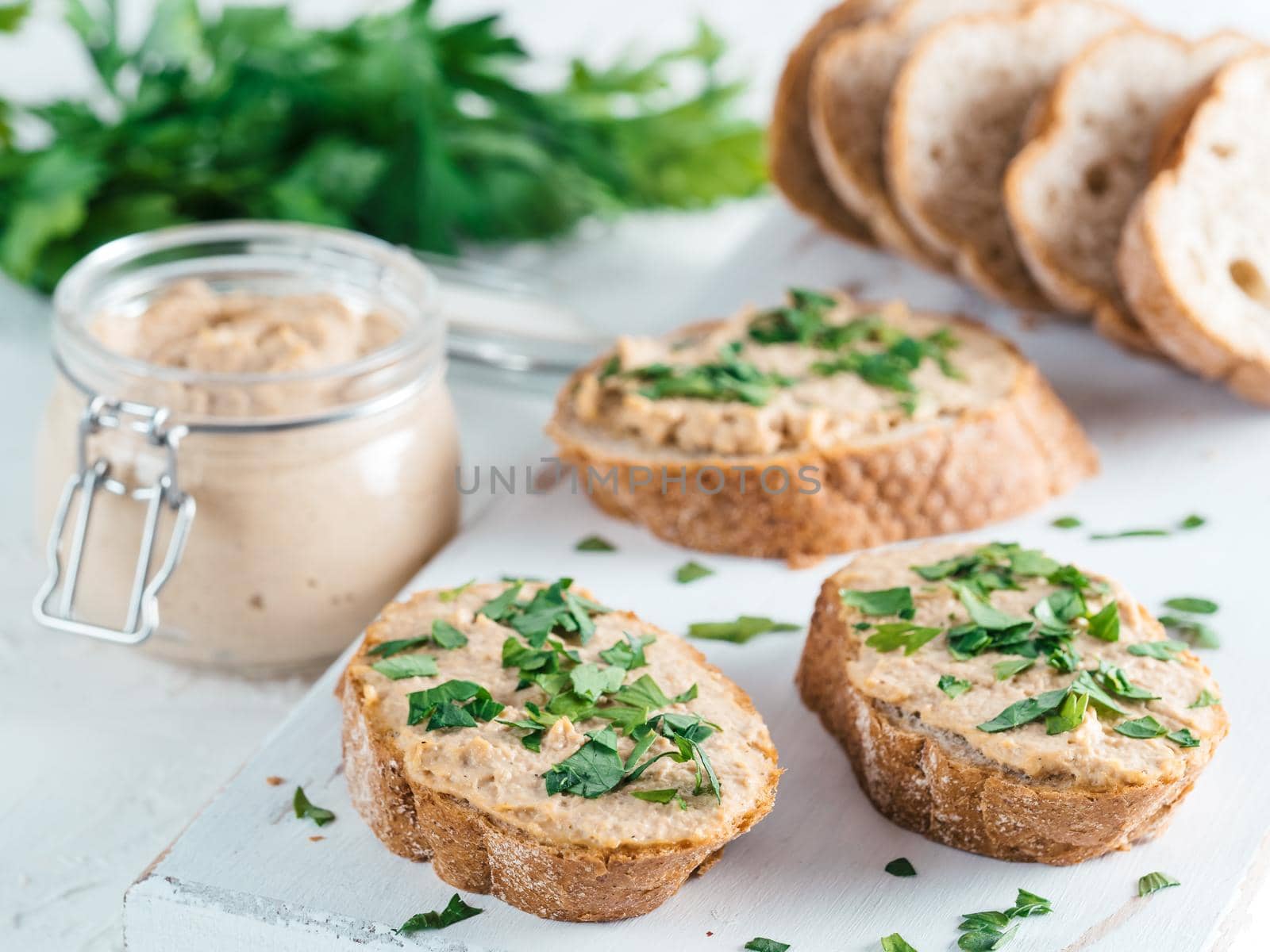 Close up view of slice bread with homemade turkey pate and fresh green parsley on white rustic kutting board over white concrete background, Shallow DOF. Selective focus