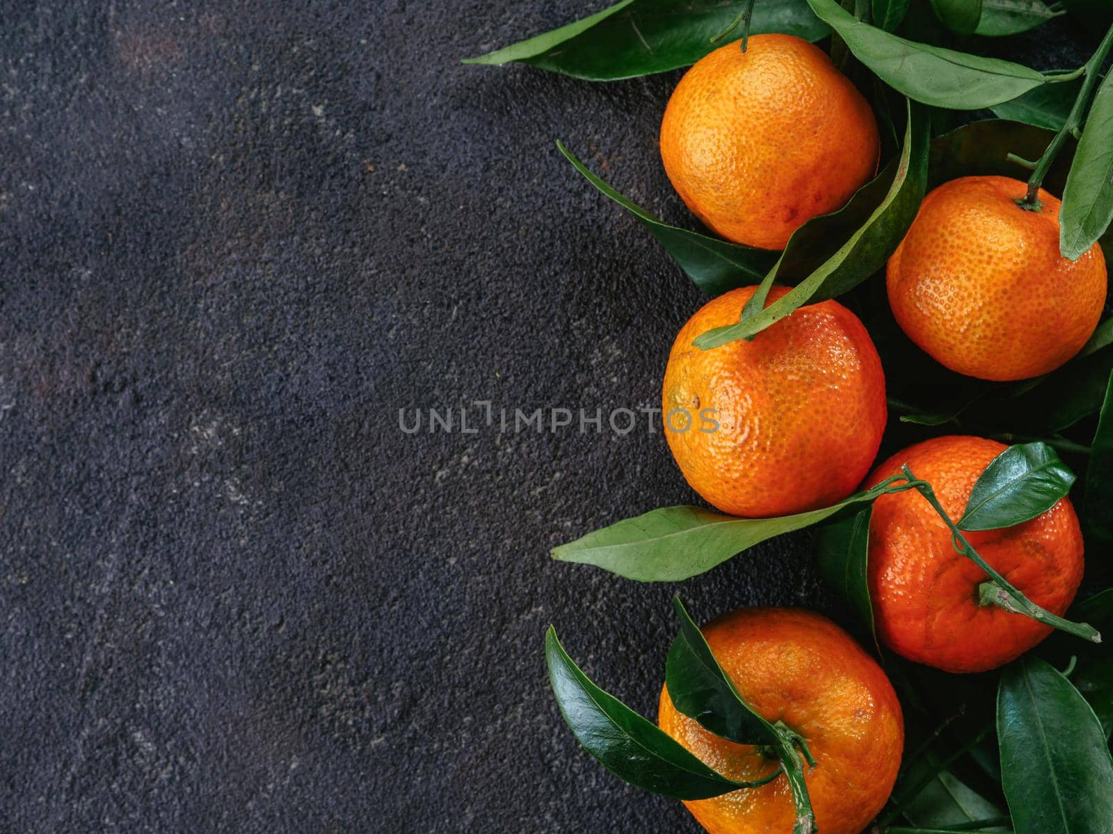 Tangerines, oranges, mandarins, clementines, citrus fruits with leaves on black cement background. Top view or flat-lay. Copy space.