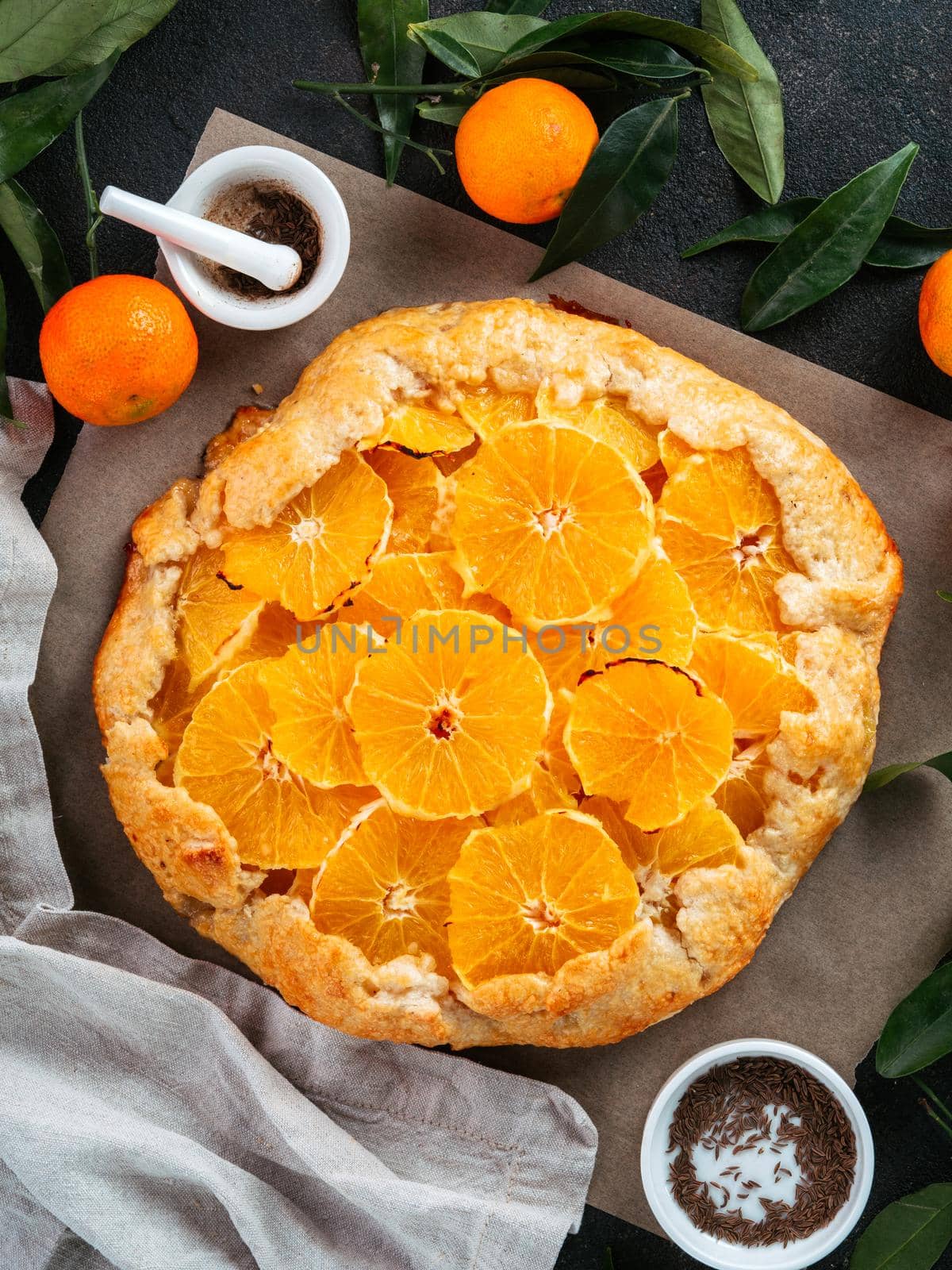 Top view of caraway and orange tart on baking paper over black cement background. Winter season and christmas ideas recipe - tart with caraway pastry and oranges, mandarines or tangerines.