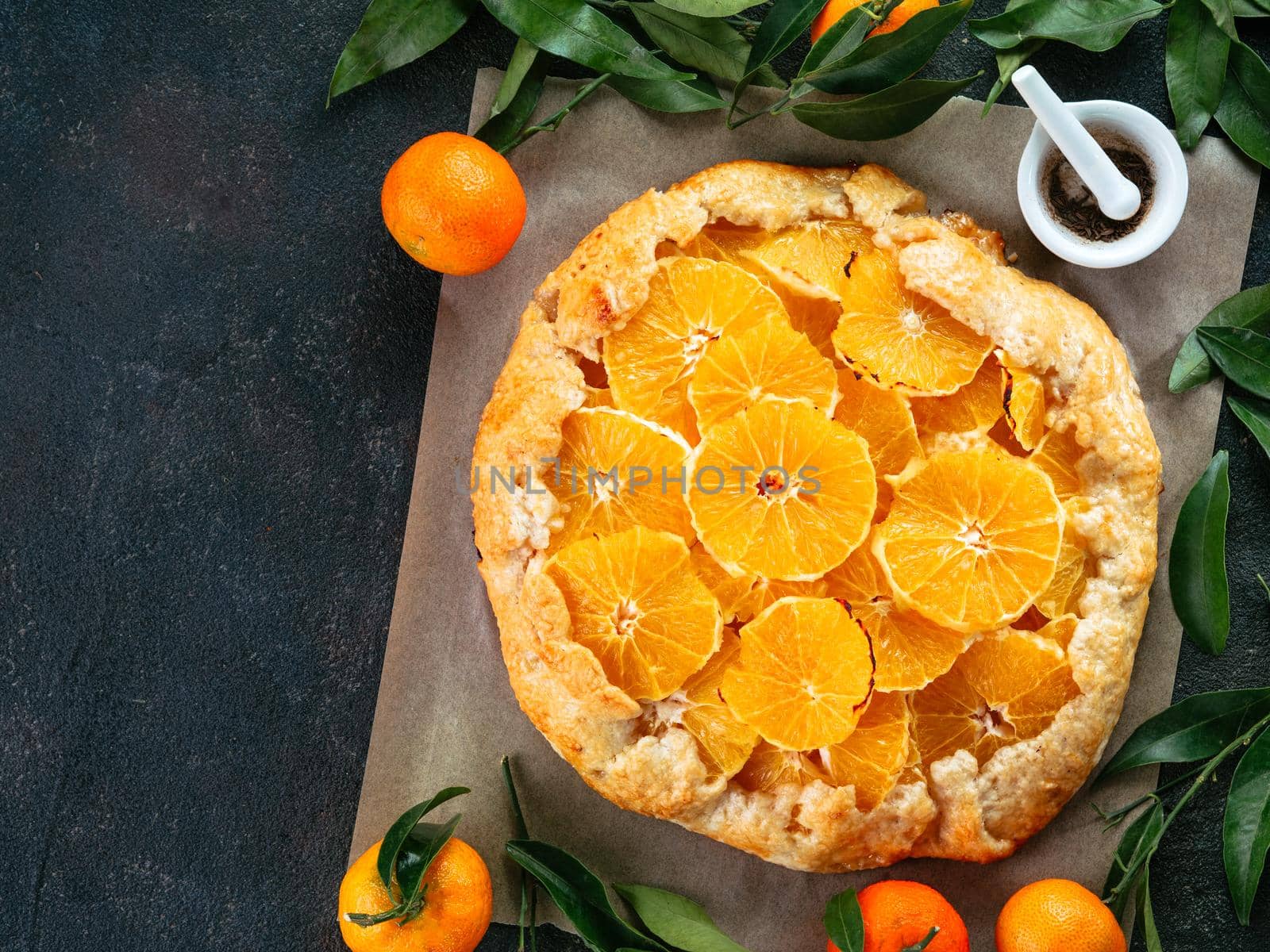 Top view of caraway and orange tart on baking paper over black cement background with copy space.Winter season and christmas ideas recipe-tart with caraway pastry and oranges, mandarines or tangerines
