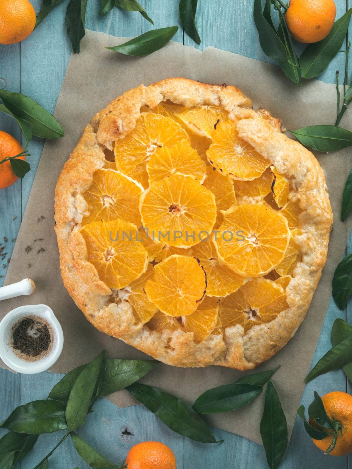 Top view of caraway and orange tart on baking paper over gray wooden table.Winter season and christmas ideas recipe-tart with caraway pastry and oranges, mandarines or tangerines