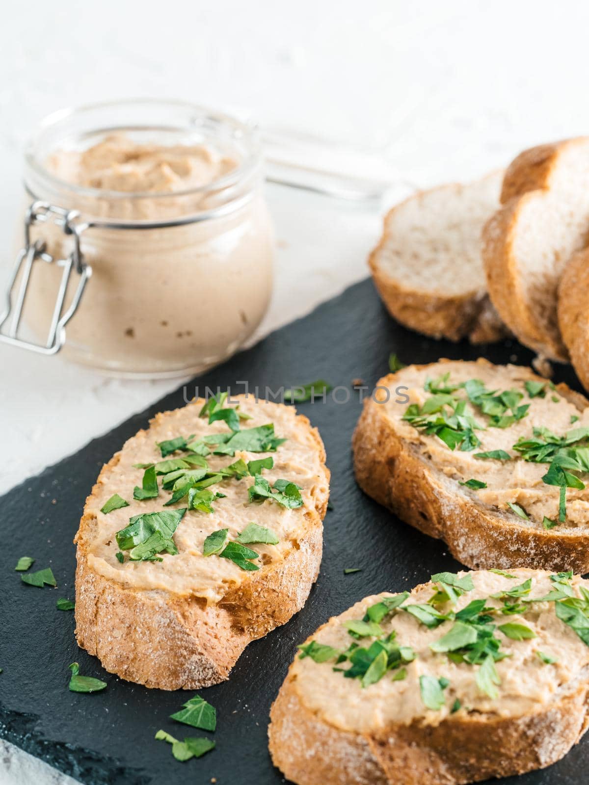 Close up view of slice bread with homemade turkey pate and fresh green parsley on black kutting board over white concrete background, Copy space.