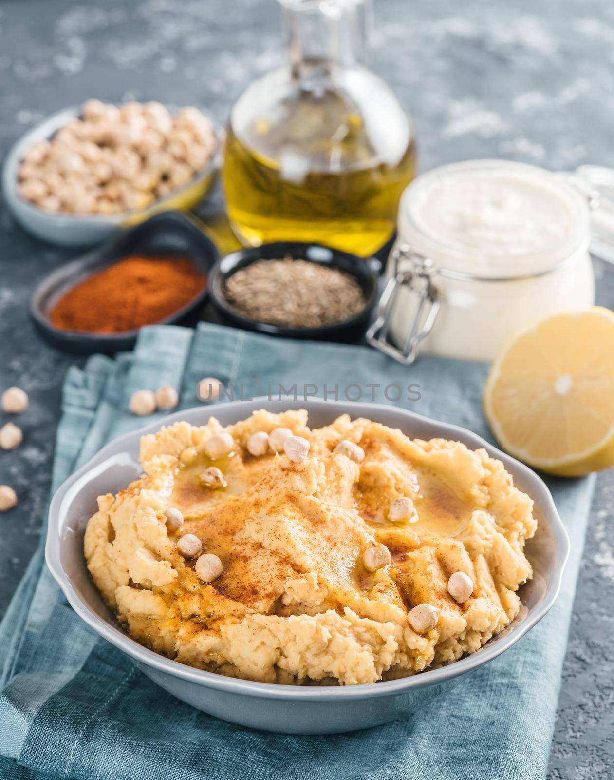 Homemade hummus with olive oil in gray bowl and ingredients. Traditional middle eastern appetizer hummus on gray background - healthy vegan paste snack. Vegetarian diet,nutrition protein food concept