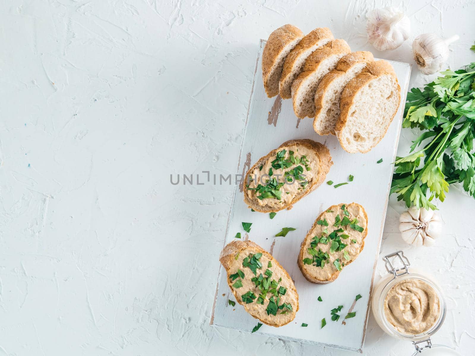 Top view of slice bread with homemade turkey pate and fresh green parsley on white rustic kutting board over white concrete background, Shallow DOF. Selective focus Copy space.
