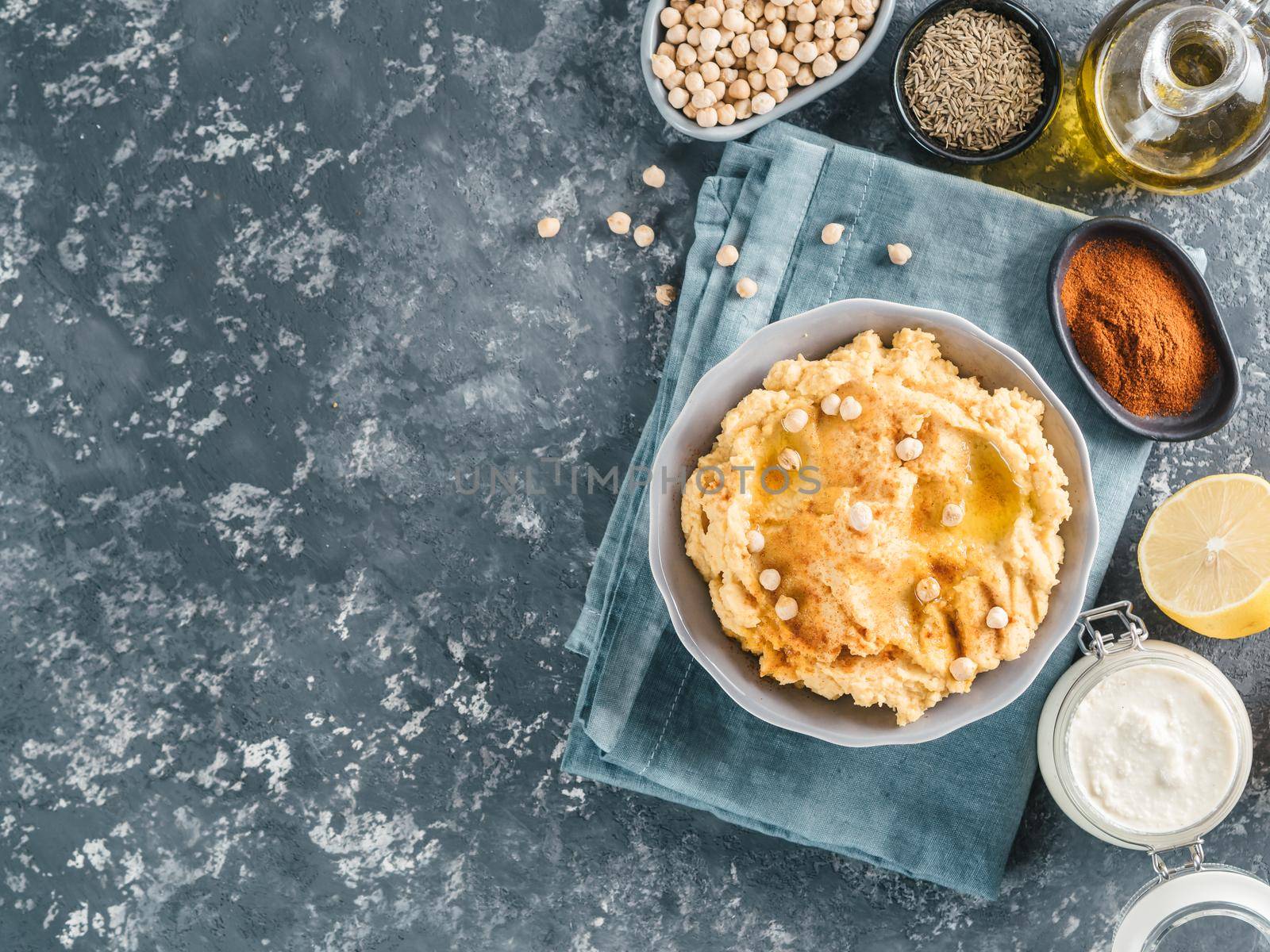 Homemade hummus in gray bowl and ingredients. Traditional middle eastern appetizer hummus on dark background - healthy vegan paste snack. Vegetarian diet,nutrition protein food concept. Copy space.