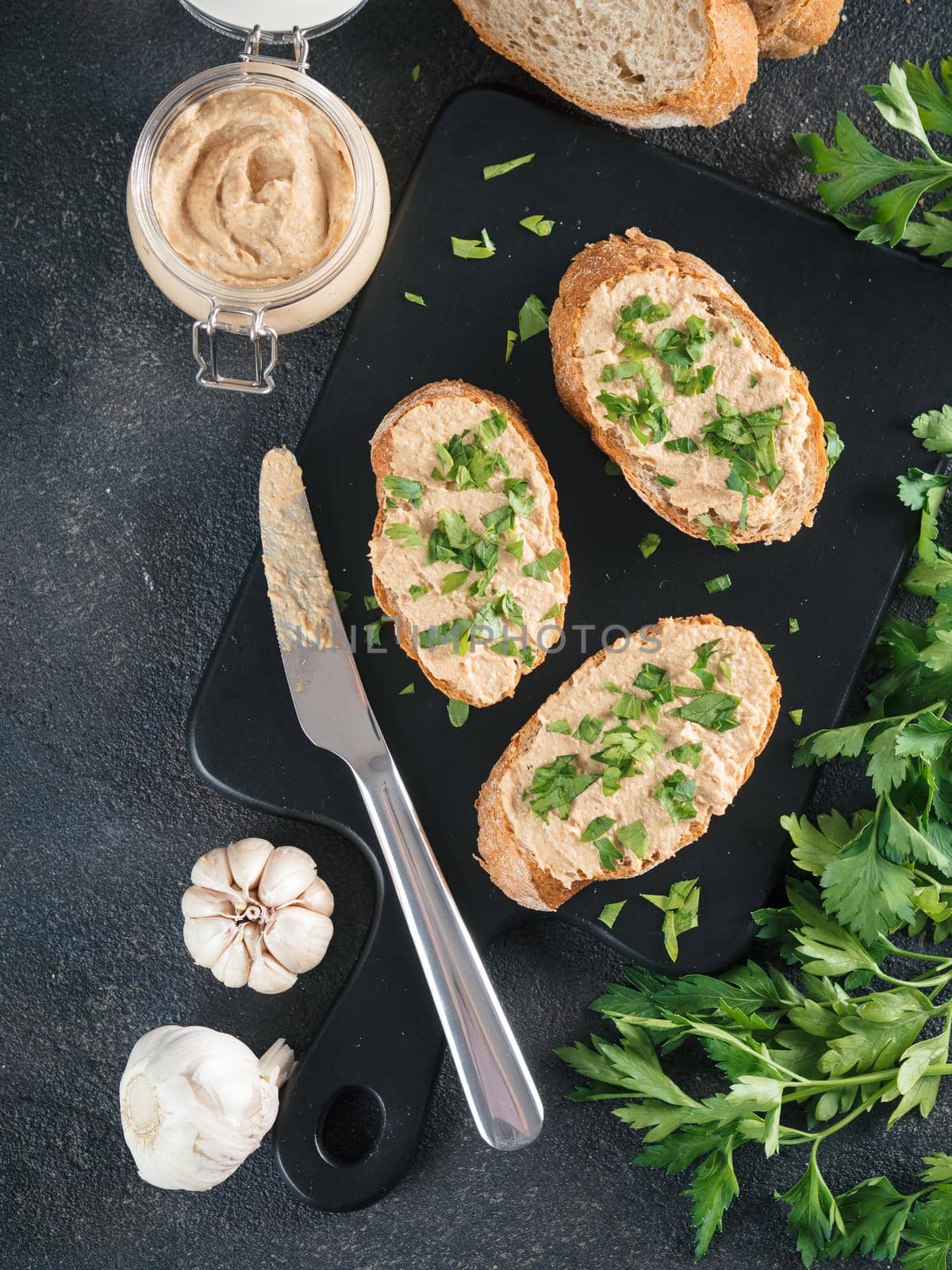 Top view of slice bread with homemade turkey pate and fresh green parsley on black kutting board over black cement background,