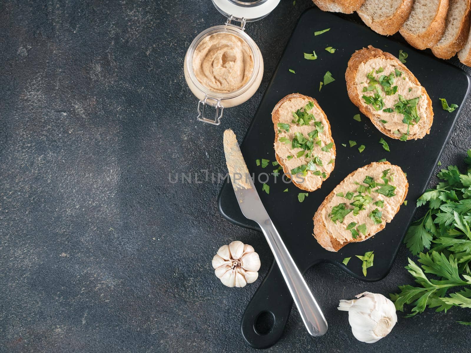 Top view of slice bread with homemade turkey pate and fresh green parsley on black kutting board over black cement background, Copy space.