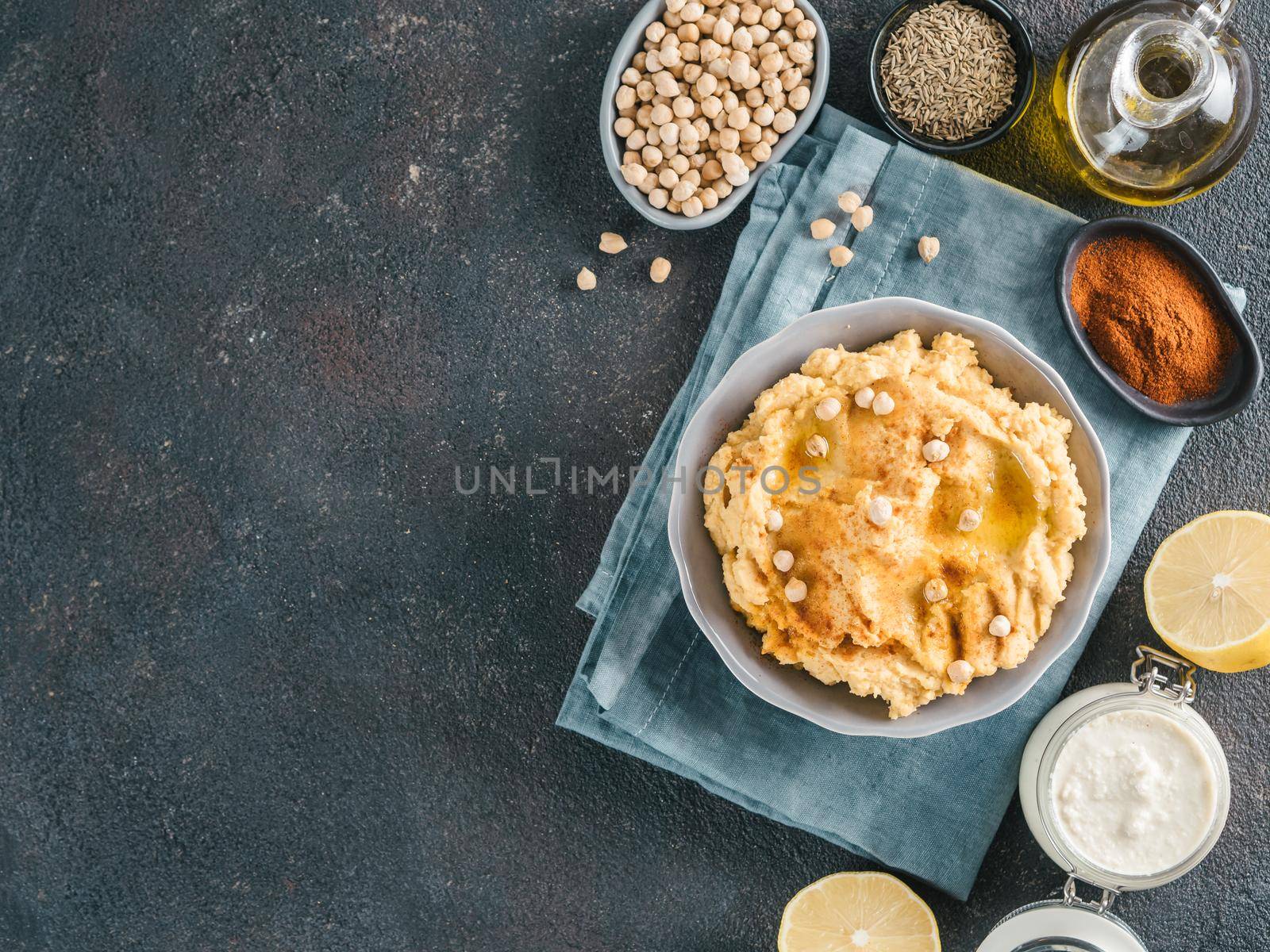 Homemade hummus in gray bowl and ingredients. Traditional middle eastern appetizer hummus on dark background - healthy vegan paste snack. Vegetarian diet,nutrition protein food concept. Copy space.