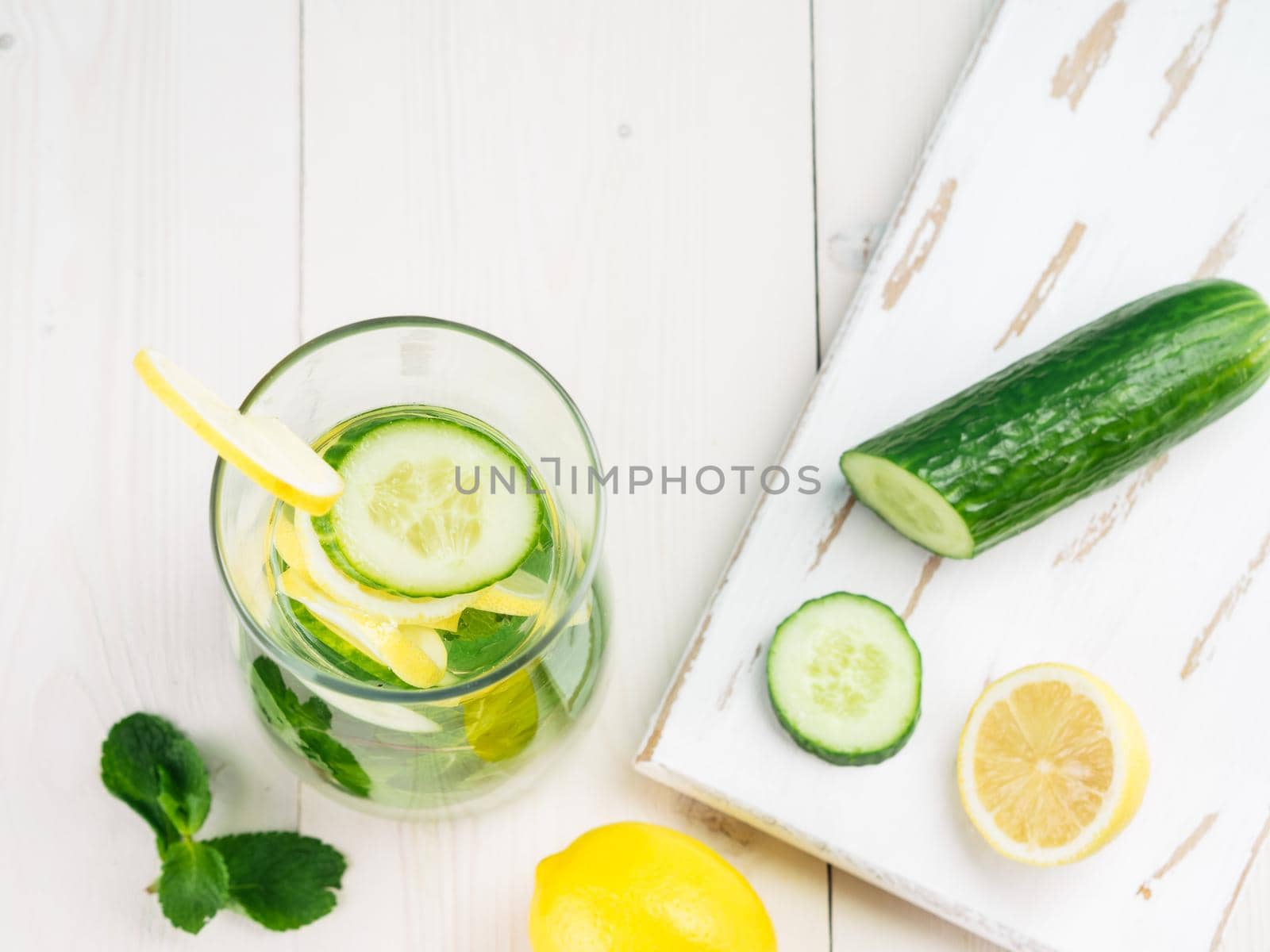 Infused detox water with cucumber, lemon and mint in glass bottle on white table. Diet, healthy eating, weight loss concept. Copy space. Top view or flat-lay.