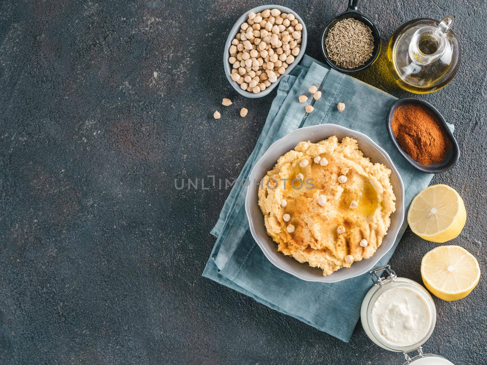 Homemade hummus in gray bowl and ingredients. Traditional middle eastern appetizer hummus on dark background - healthy vegan paste snack. Vegetarian diet,nutrition protein food concept. Copy space.