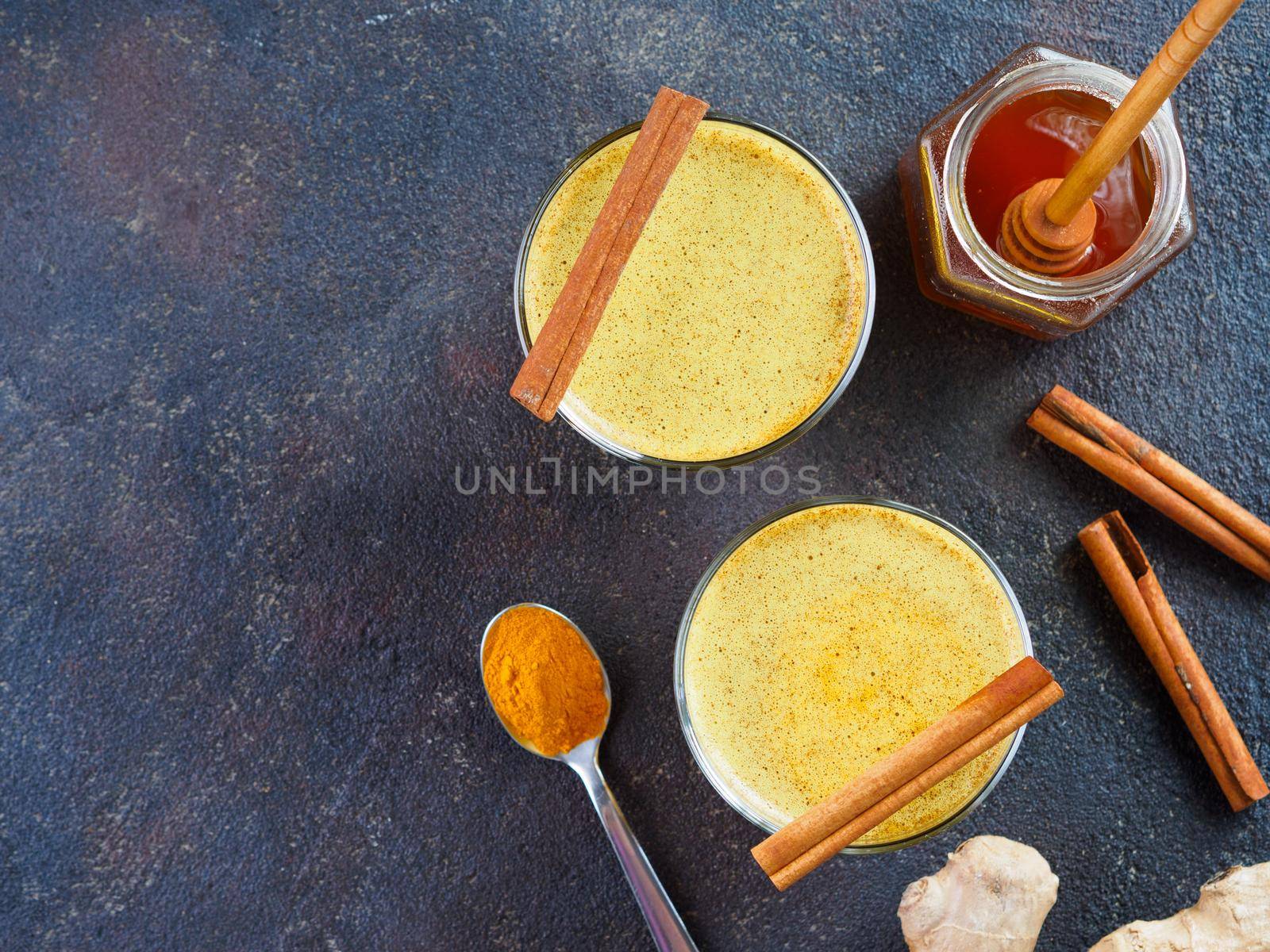 Healthy drink golden turmeric latte in glass.Gold milk with turmeric,ginger root,cinnamon sticks,turmeric powder and honey on black background.Detox turmeric tea and ingredients. Copy space. Top view