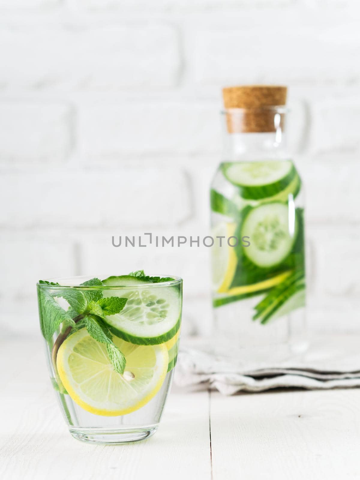 Infused detox water with cucumber, lemon and mint in glass and bottle on white table. Diet, healthy eating, weight loss concept. Copy space