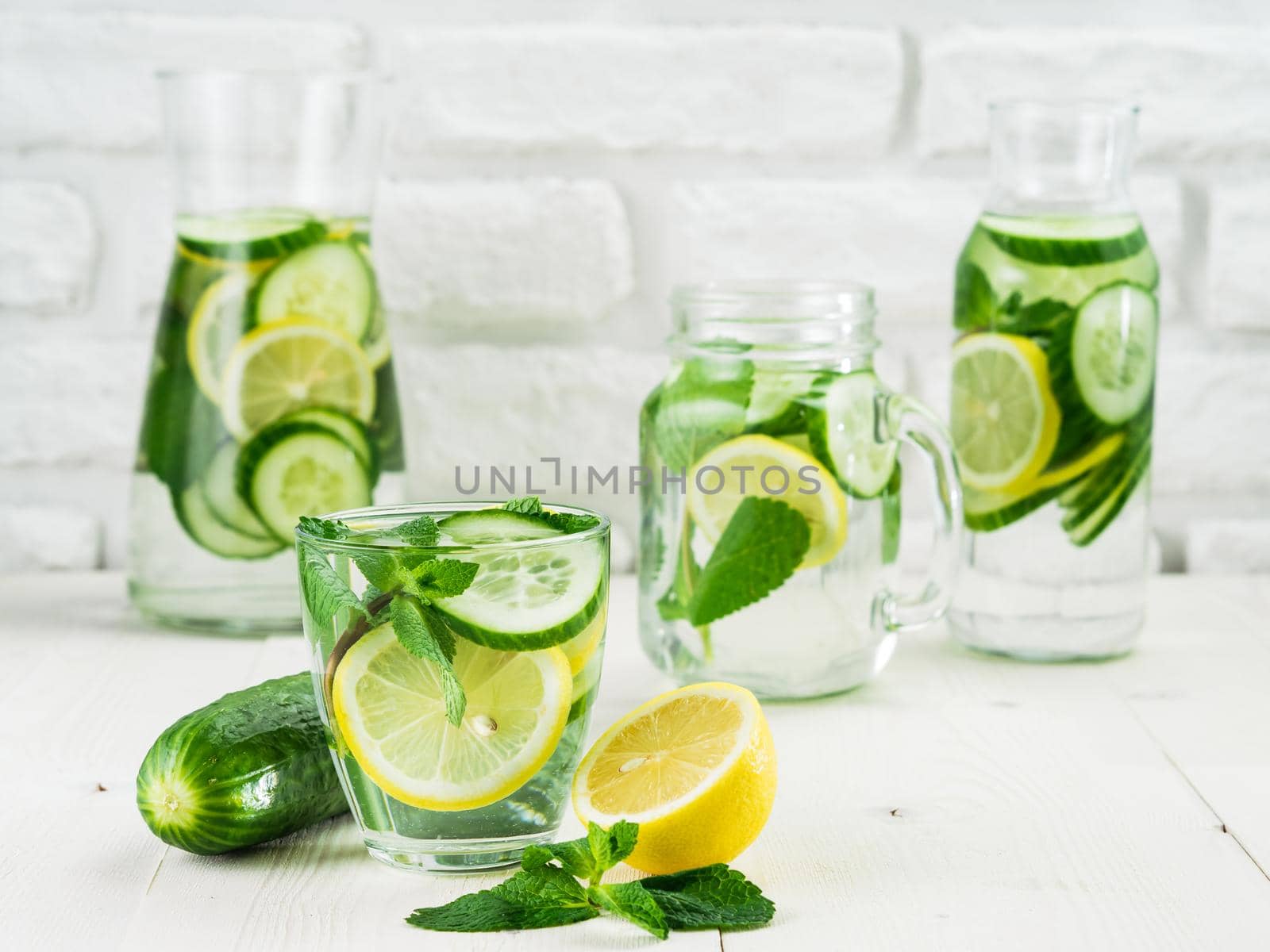 Infused detox water with cucumber, lemon and mint in different glass bottles on white table. Diet, healthy eating, weight loss concept. Copy space