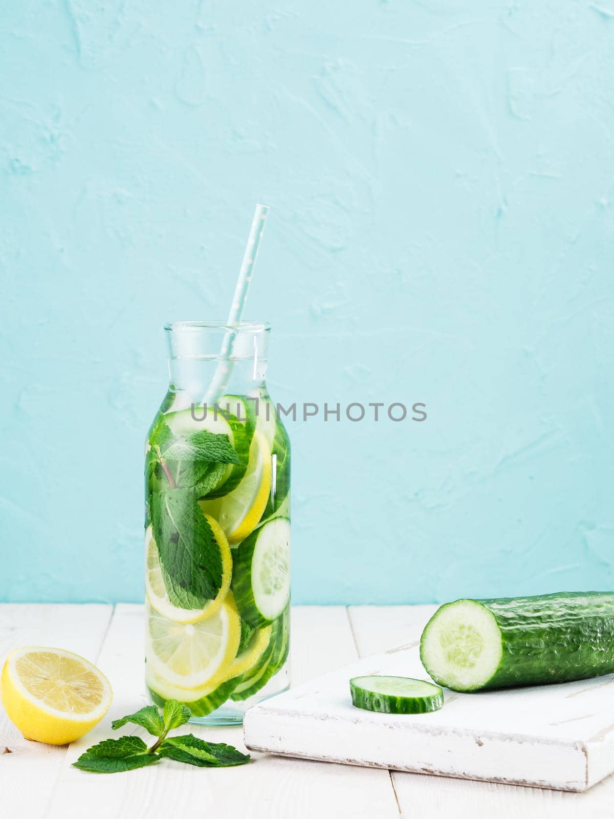 Infused detox water with cucumber, lemon and mint in glass bottle on white table. Diet, healthy eating, weight loss concept. Copy space