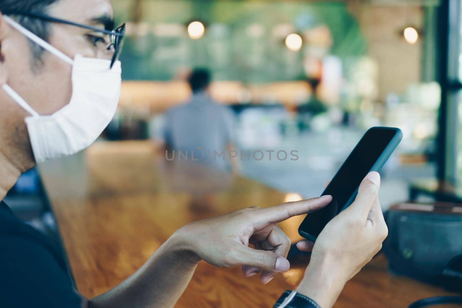 Man wear mask in public area and using smartphone to do work business, social network, communication in public cafe work space area.