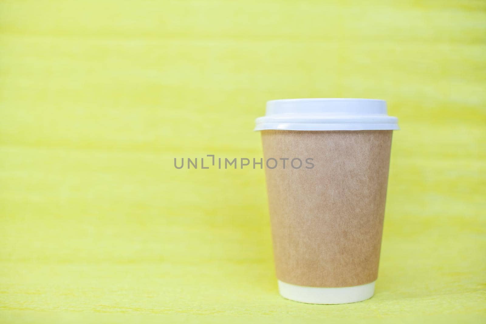 Paper cup of coffee closed with a white lid on a yellow background. There is a place for the text.