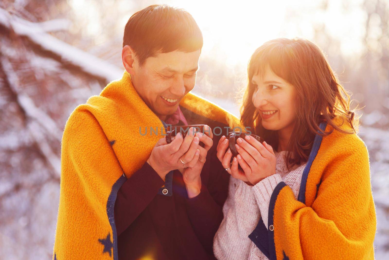 Young couple in love holding mugs with hot tea in winter forest.