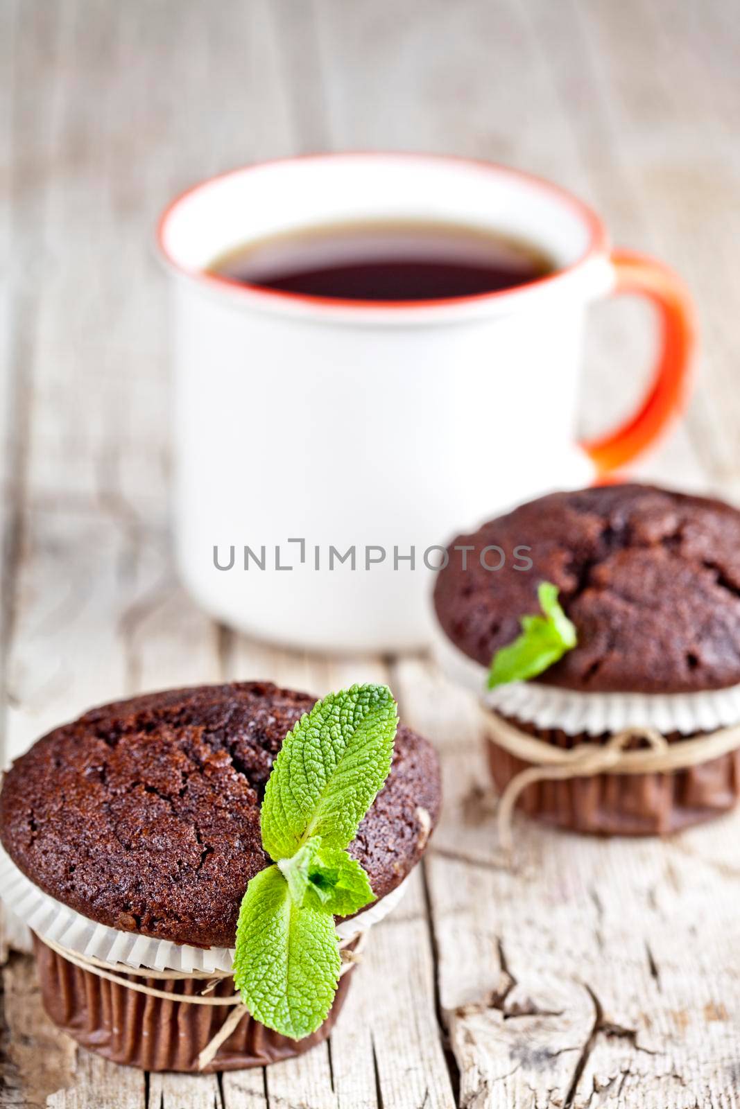Fresh dark chocolate muffins with mint leaves and cup of tea on rustic wooden table. by marylooo