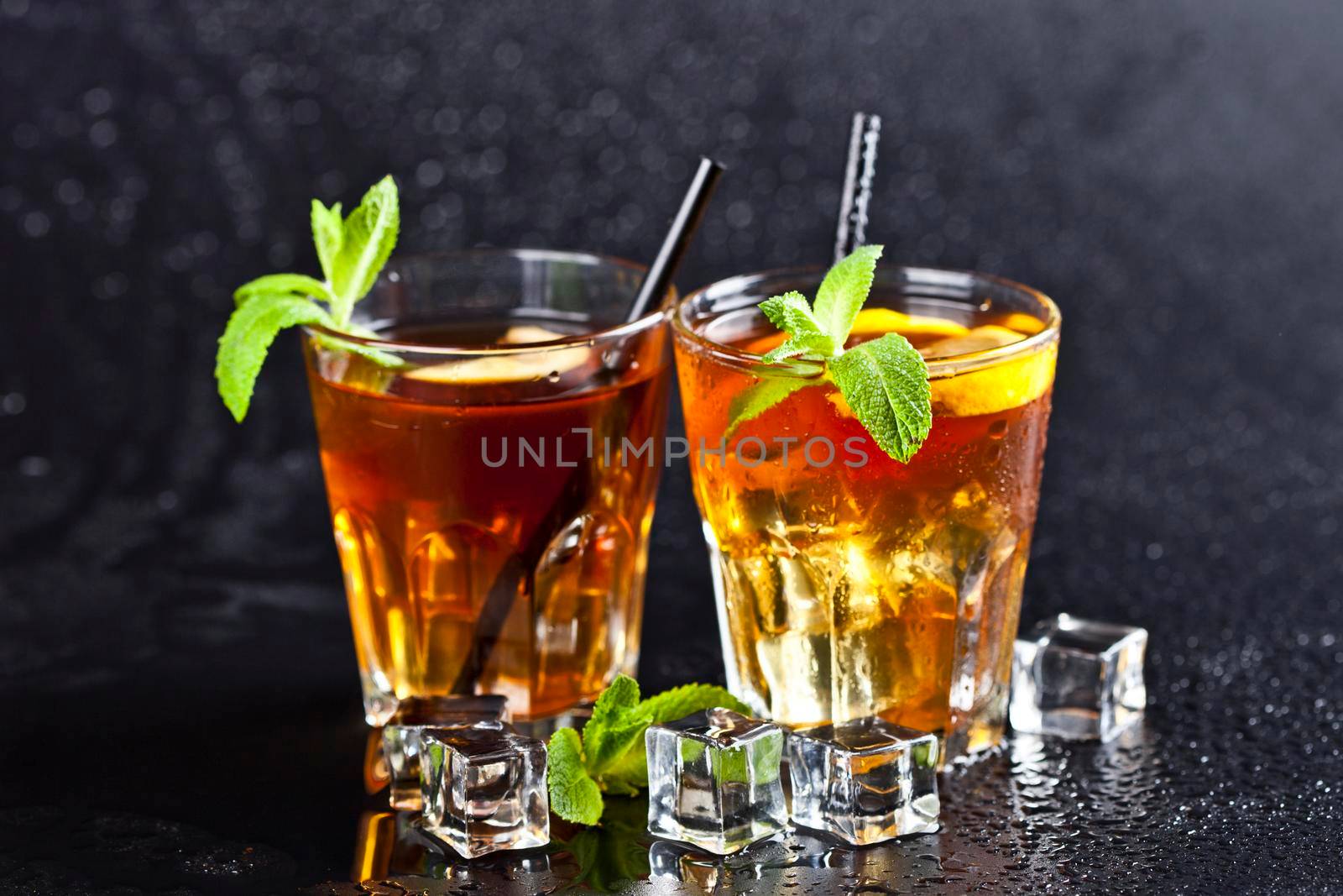 Two glasses with cold traditional iced tea with lemon, mint leaves and ice cubes by marylooo