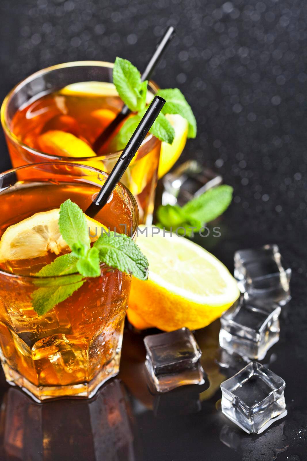 Two glasses with cold traditional iced tea with lemon, mint leaves and ice cubes by marylooo