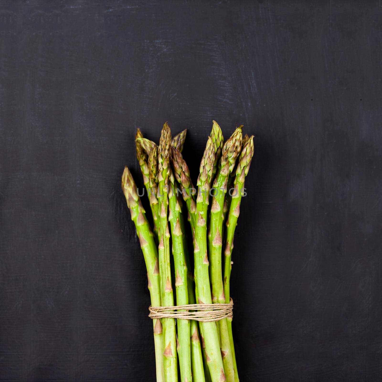 Bunch of fresh raw garden asparagus on black board background. by marylooo