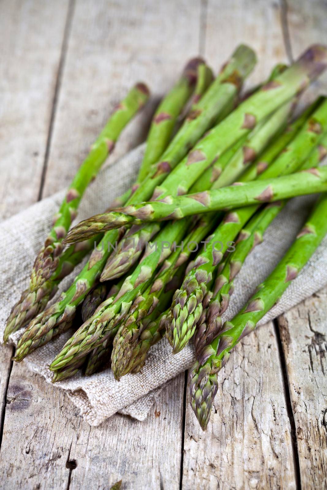 Bunch of fresh raw garden asparagus closeup and linen napkin on rustic wooden table background. by marylooo