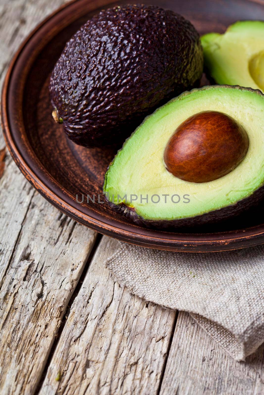 Fresh organic avocado on ceramic plate and linen napkin on rustic wooden table background. by marylooo