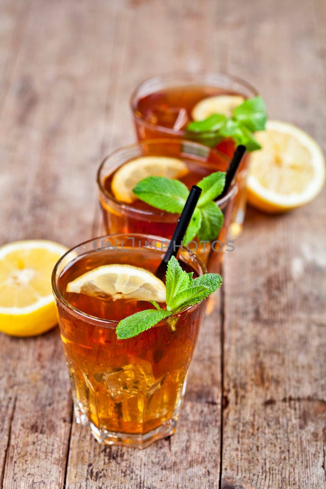 Cold iced tea with lemon, mint leaves and ice cubes in three glasses on rustic wooden table. by marylooo