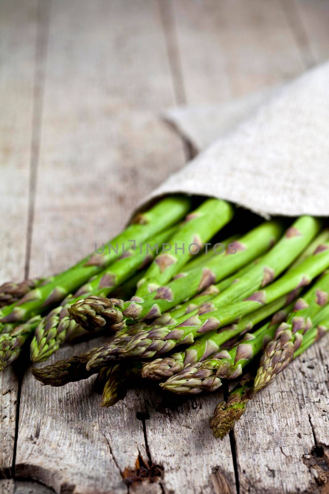Bunch of fresh raw garden asparagus closeup and linen napkin on rustic wooden table background.  by marylooo