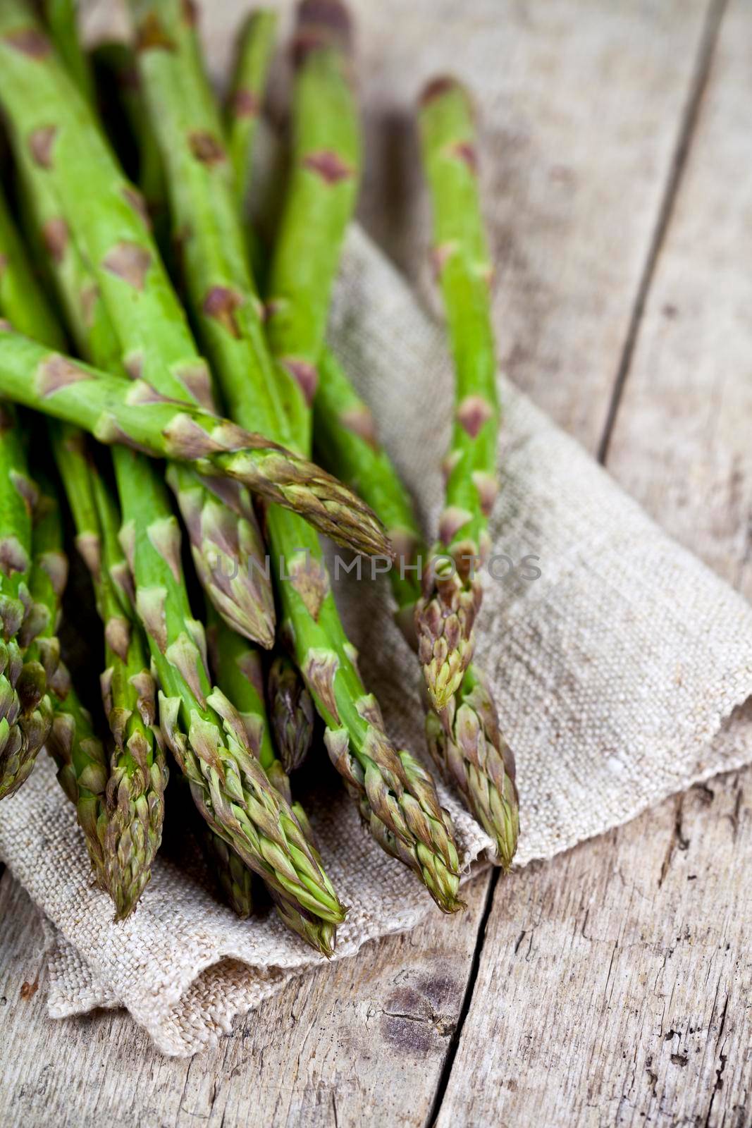 Bunch of fresh raw garden asparagus closeup and linen napkin on rustic wooden table background by marylooo