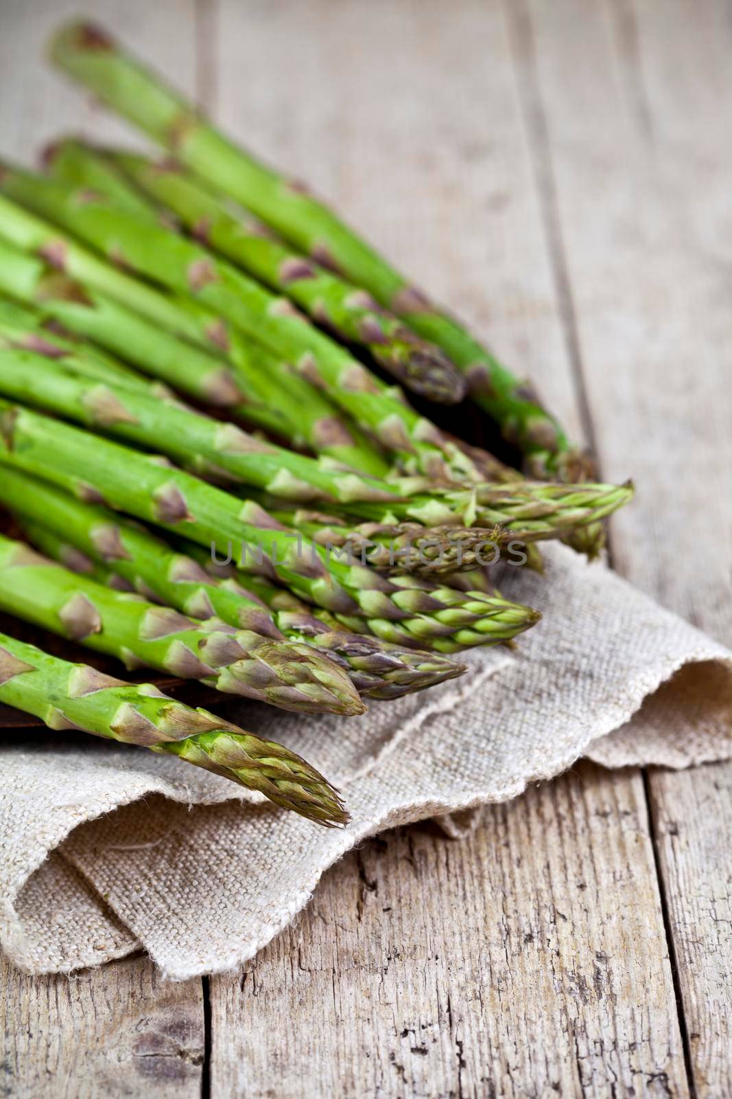 Bunch of fresh raw garden asparagus closeup and linen napkin on rustic wooden table background. by marylooo