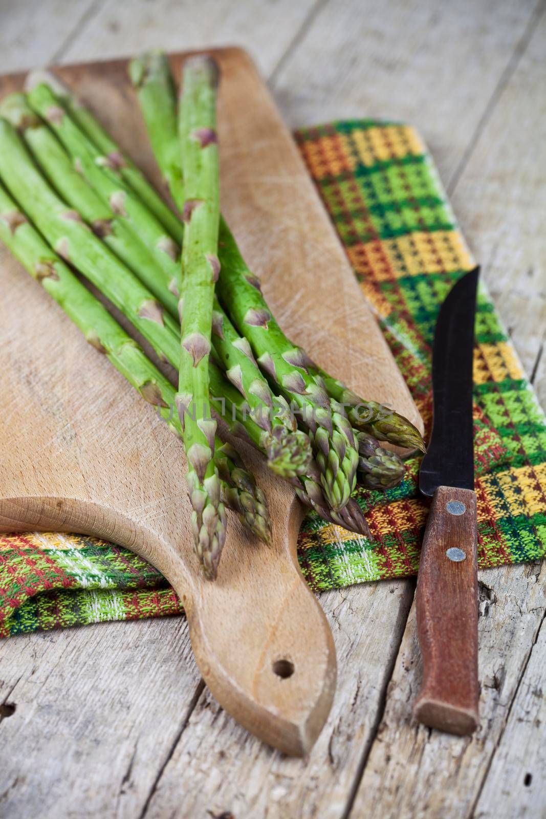Raw garden asparagus and knife closeup on cutting board on rustic wooden table background.  by marylooo
