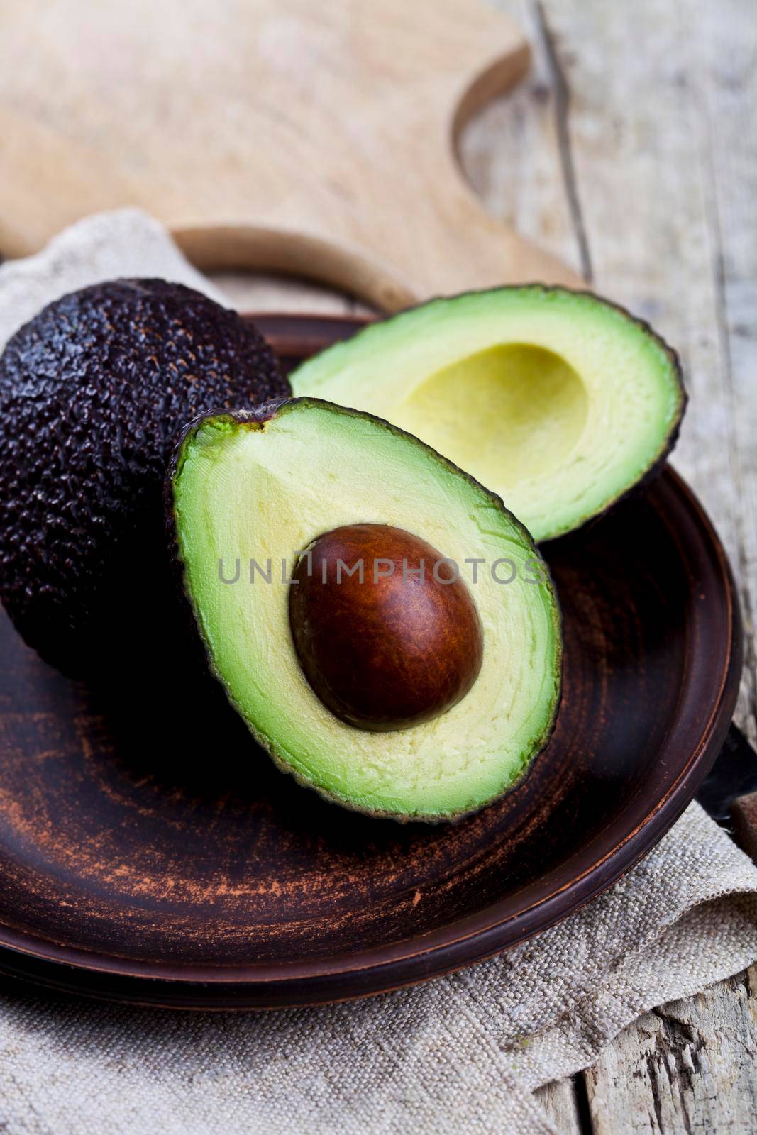 Fresh organic avocado on ceramic plate and linen napkin on rustic wooden table background.  by marylooo