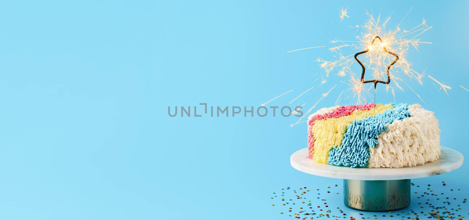 Shag cake with burned sparkler star on blue background. Colorful shag cake with perfect vanilla buttercream. Idea of visually striking cake decorating trendy cake, copy space. Long horizontal banner.