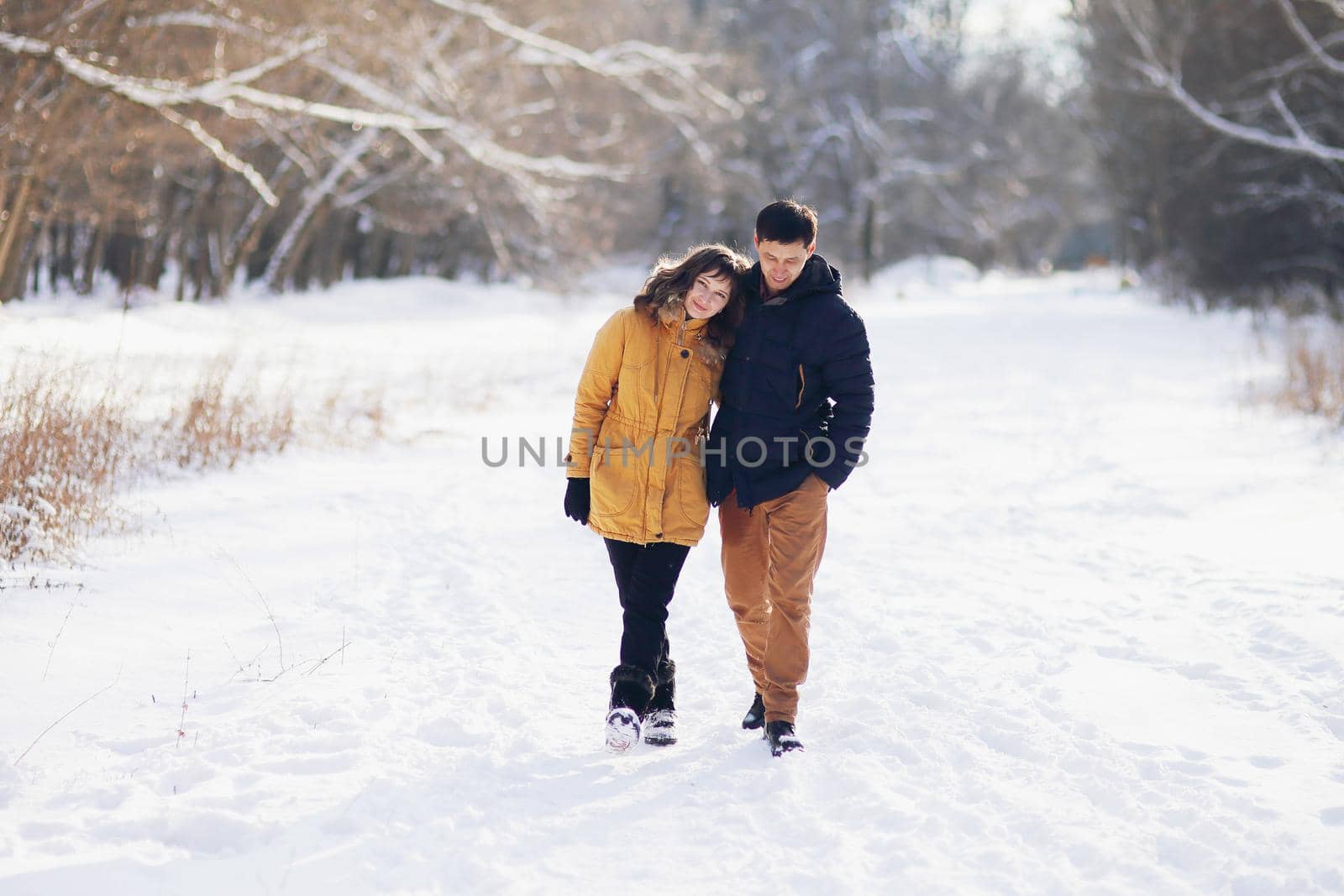On a winter day, a young couple is walking in an embrace in the park and communicating.