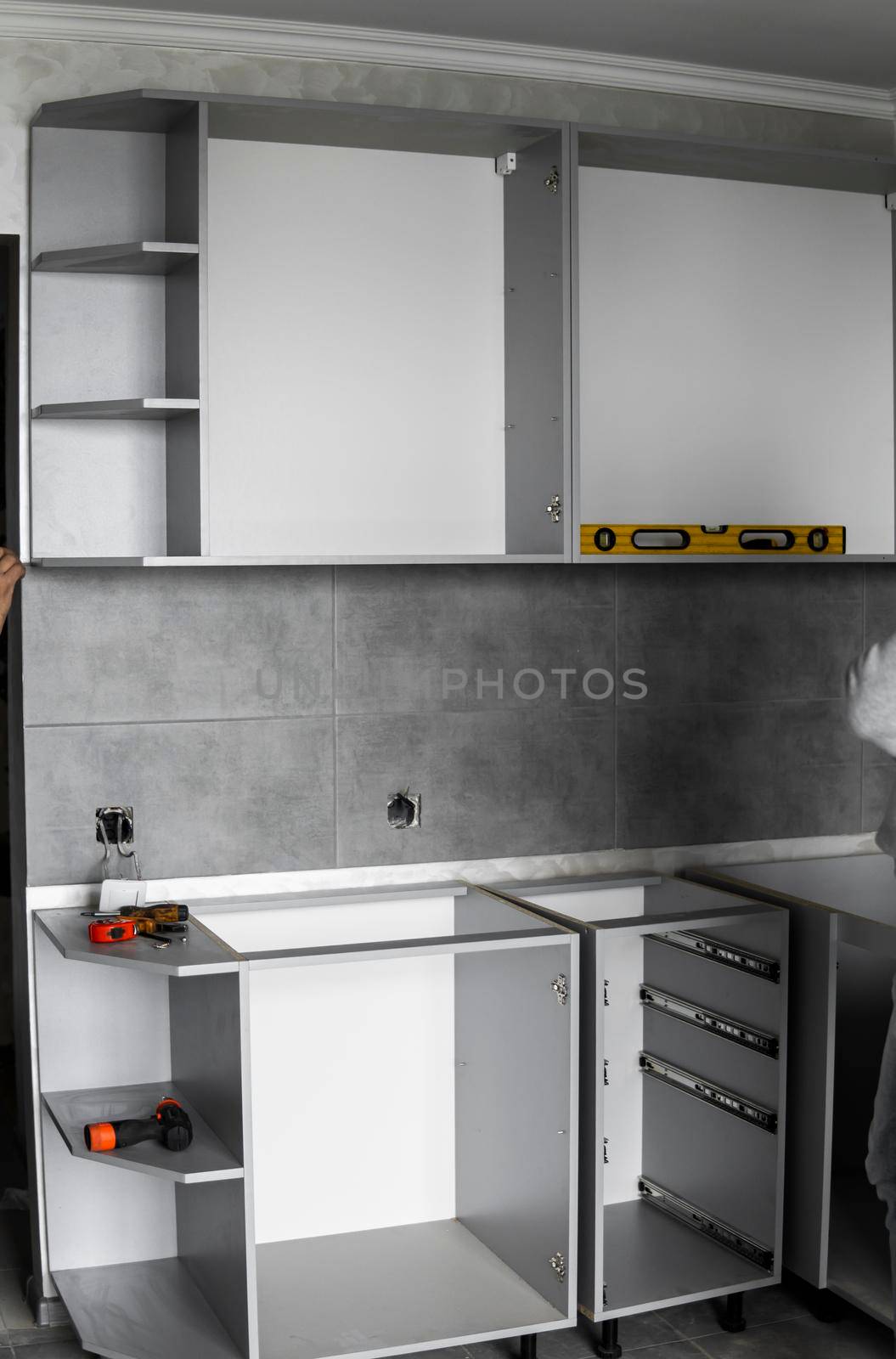 Custom kitchen cabinets installation without a furniture facades mdf. Gray modular kitchen from chipboard material on a various stages of installation in kitchen with a grey tile on floor and walls. by vovsht