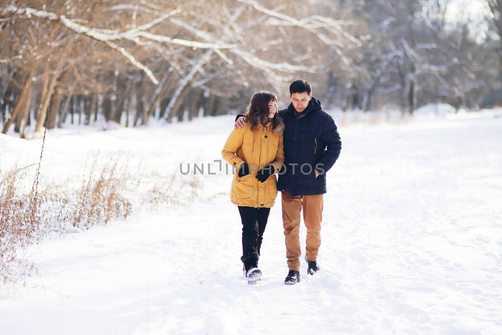 On a winter day, a young couple is walking in an embrace in the park and communicating.