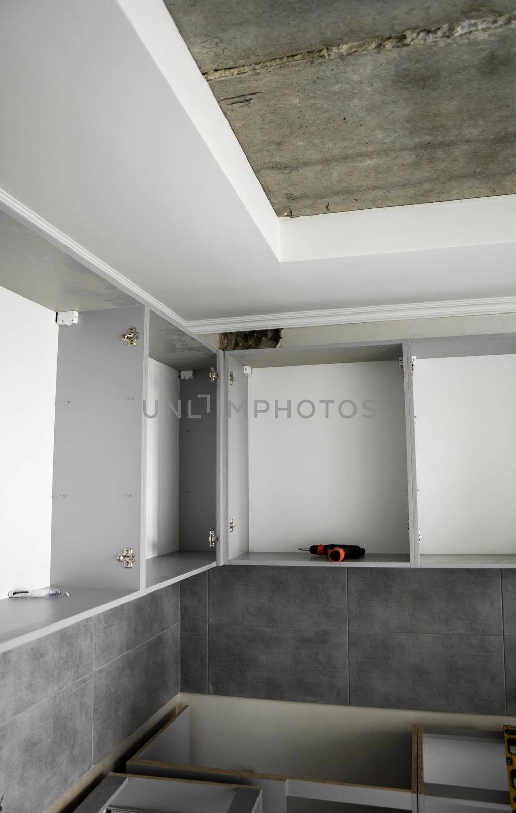 Custom kitchen cabinets installation without a furniture facades mdf. Gray modular kitchen from chipboard material on a various stages of installation in kitchen with a grey tile on floor and walls. by vovsht
