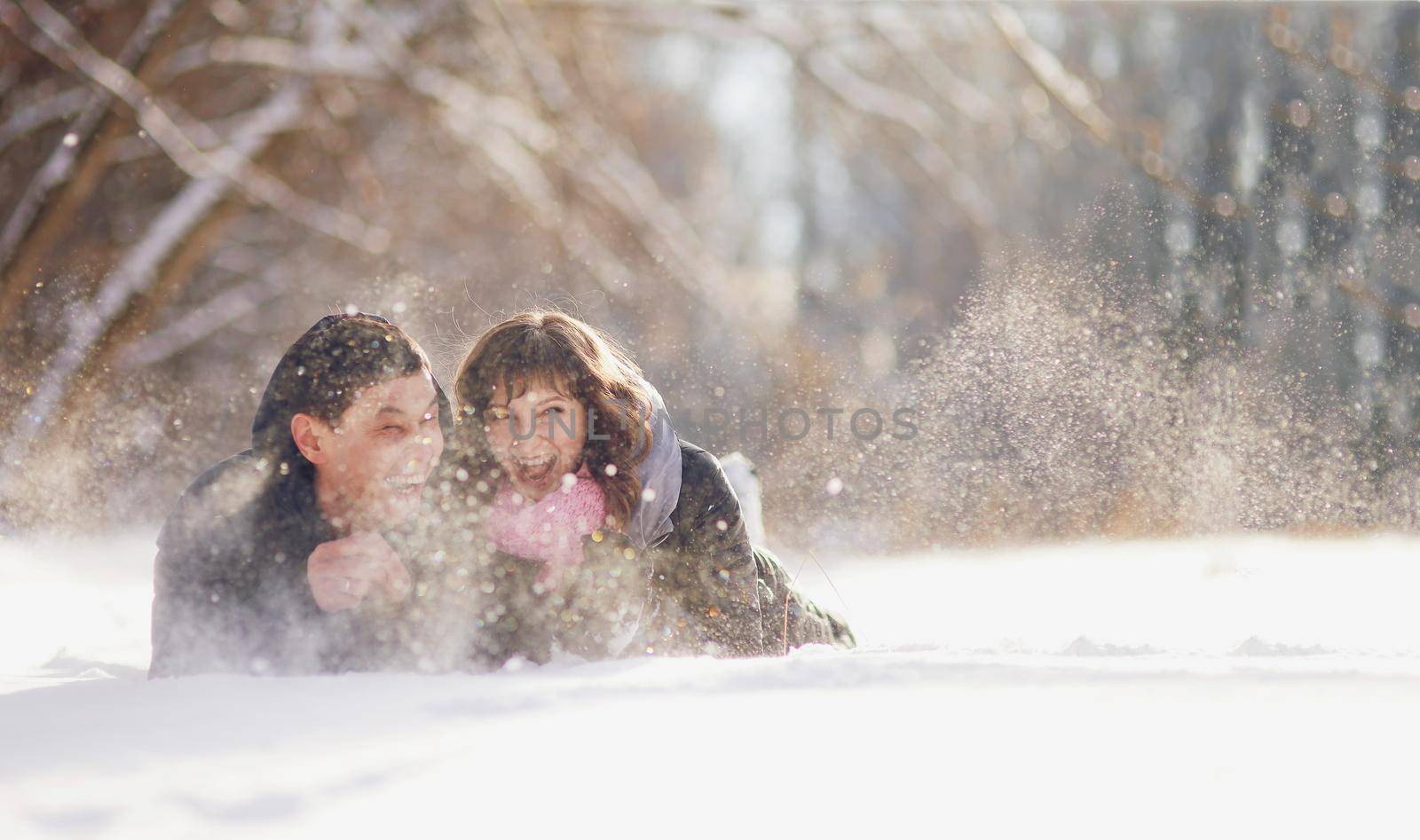 Happy couple lying on the snow and laughing by selinsmo