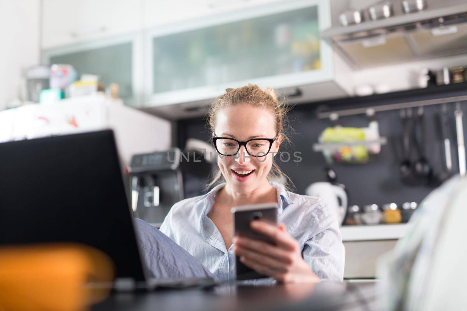 Stay at home and social distancing. Woman in her casual home clothing working remotly from kitchen dining table. Video chatting using social media with friend, family, business clients or partners.