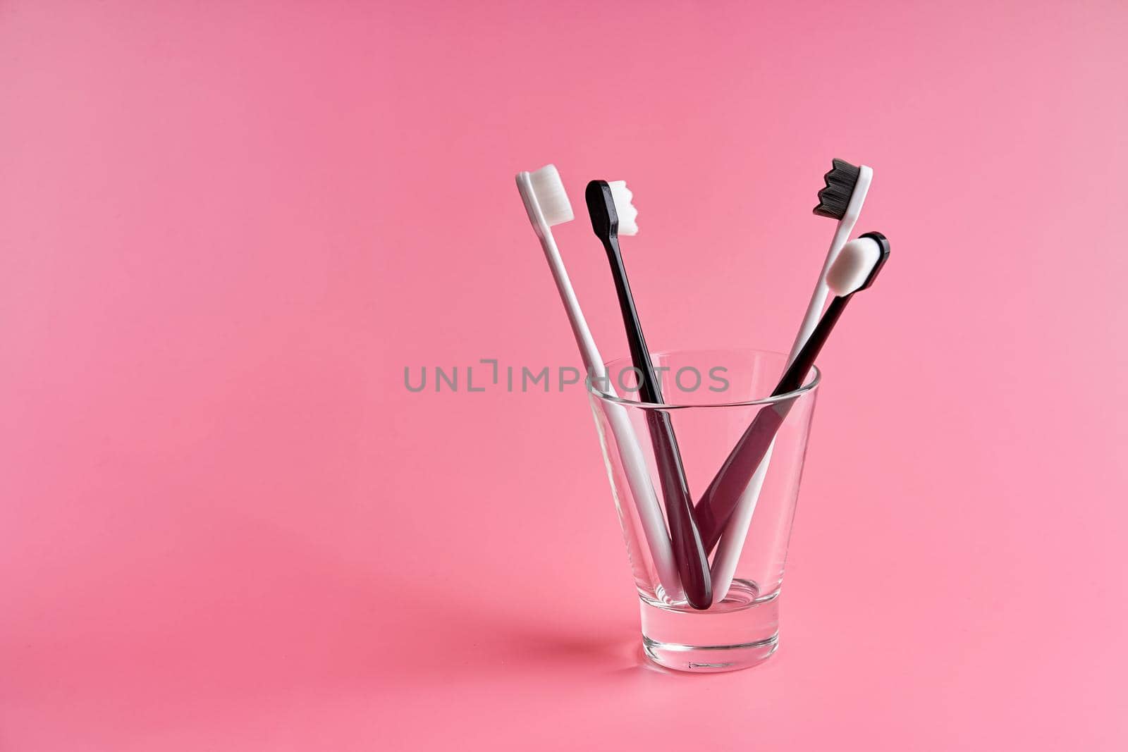 Fashionable toothbrush with soft bristles. Popular toothbrushes. Hygiene trends. Kit of toothbrushes in glass on pink background by Try_my_best