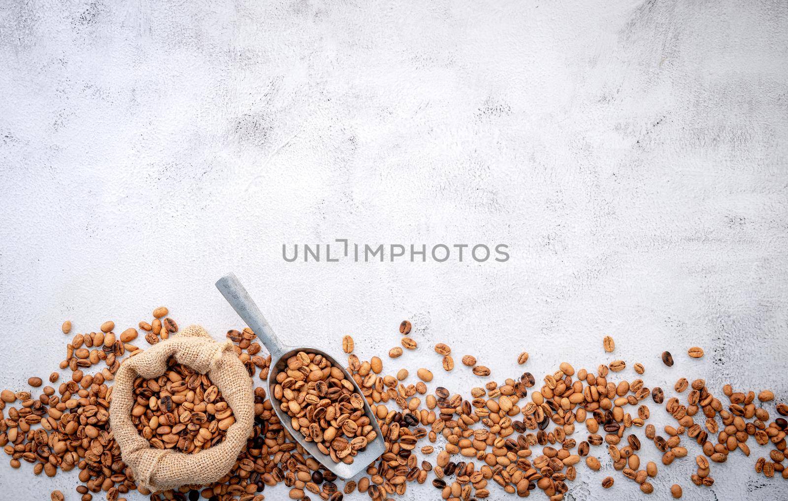 Roasted coffee beans with scoops setup on white concrete background.